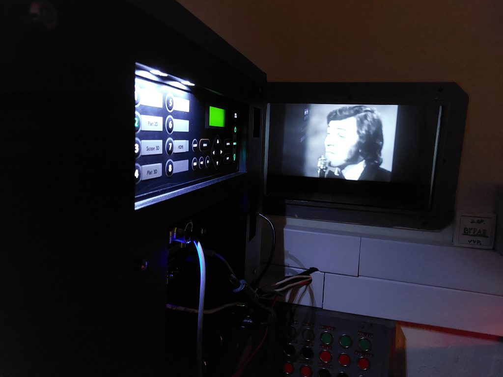 Od promítacího přístroje vidíme skrz zvukotěsné okno do sálu, kde se promítá film.